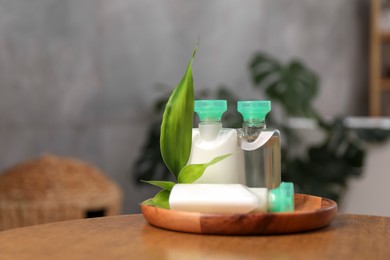 Photo of Mini bottles of cosmetic products and green branch on wooden table against blurred background. Space for text