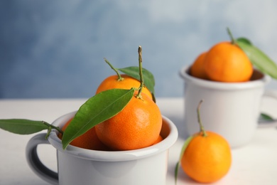 Fresh ripe tangerines with green leaves in cup on table, closeup