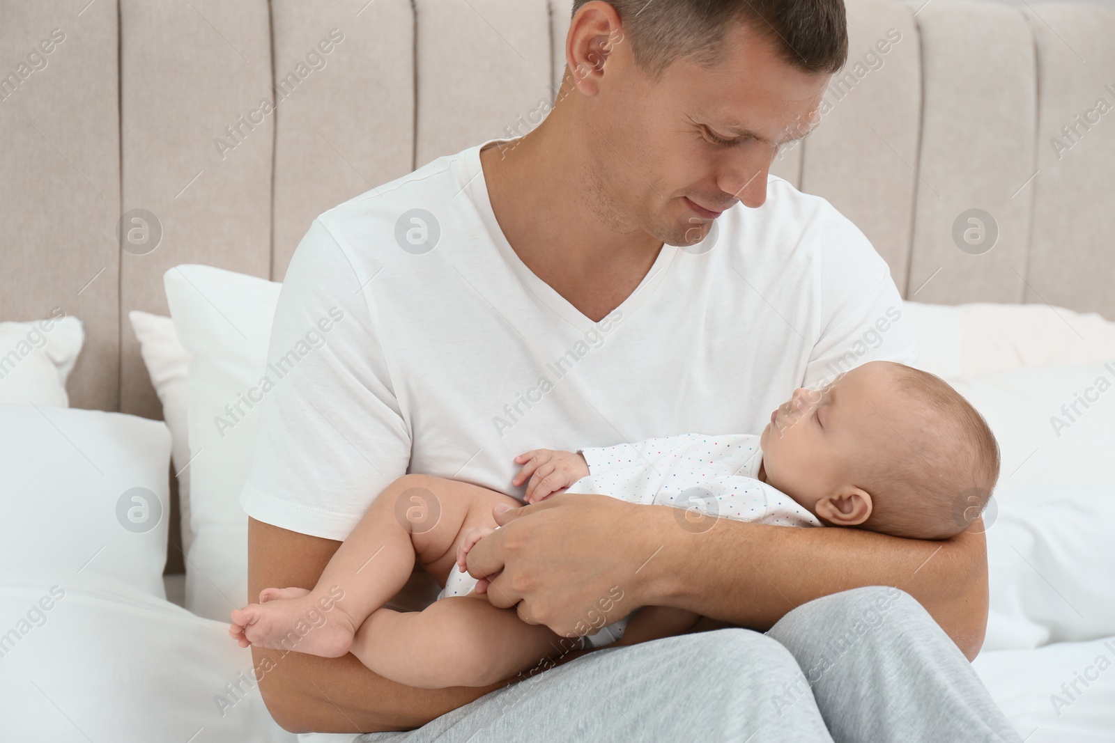 Photo of Happy father holding his cute sleeping baby on bed at home