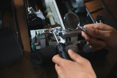 Photo of Repairman with magnifying glass and screwdriver fixing modern printer, closeup