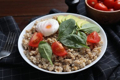 Photo of Delicious boiled oatmeal with poached egg, tomato, avocado and fork on table, closeup