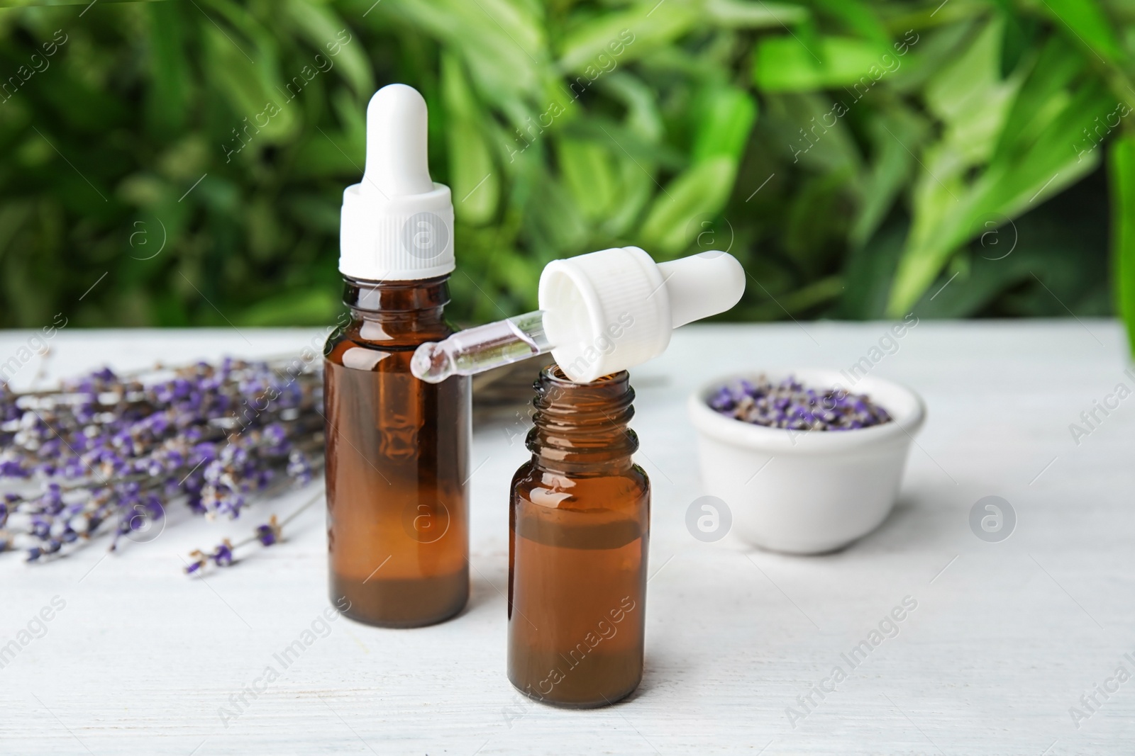 Photo of Natural herbal oil in glass bottles and lavender flowers on wooden table against blurred background