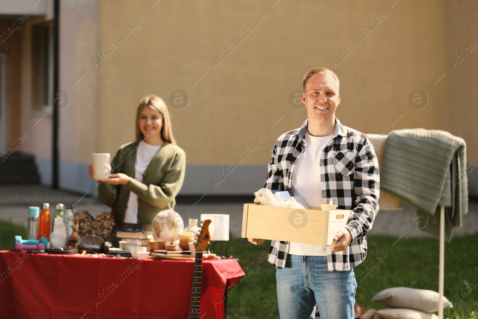Photo of Man with wooden crate and woman near table of different items in yard