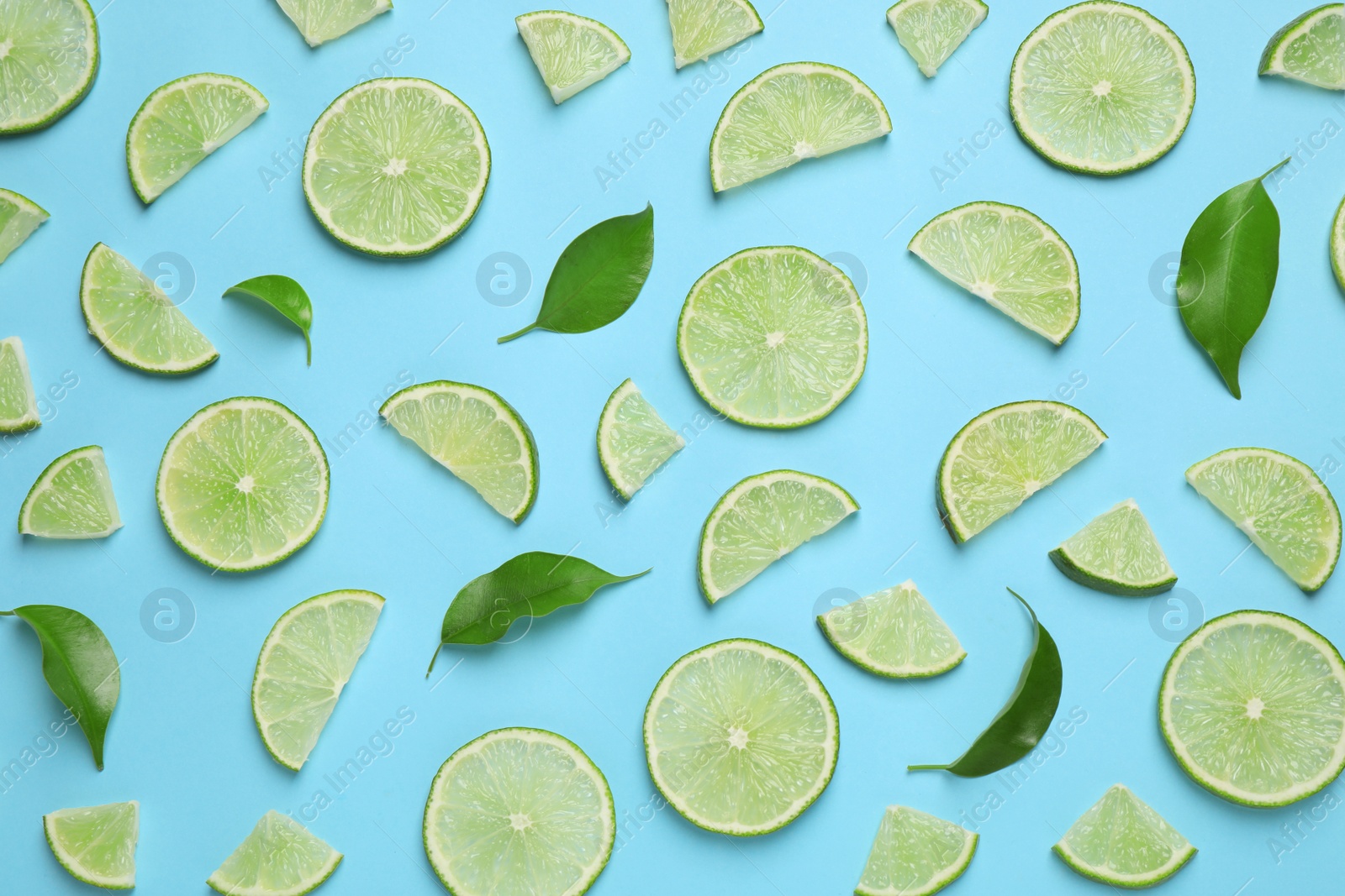 Photo of Juicy fresh lime slices and green leaves on light blue background, flat lay