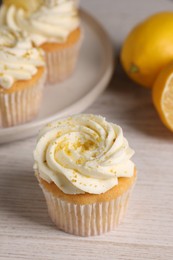 Delicious cupcakes with white cream and lemon zest on light wooden table, closeup