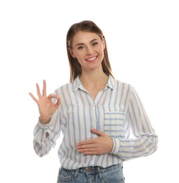 Photo of Healthy woman holding hand on belly and showing OK gesture against white background