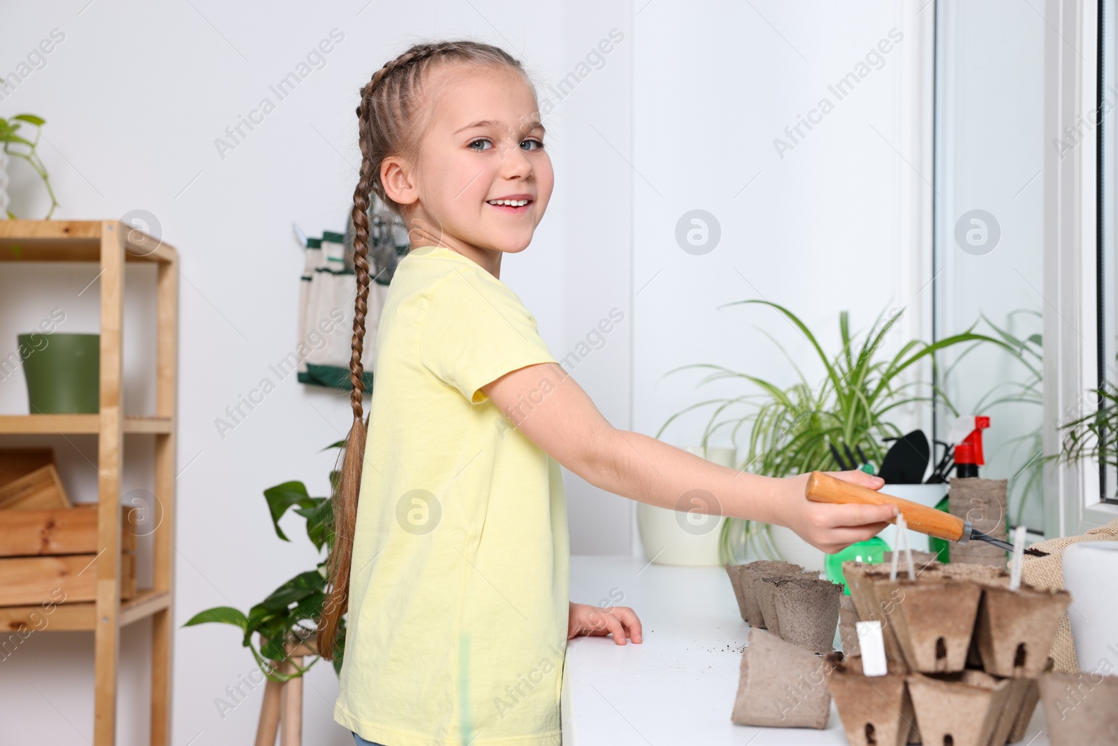 Photo of Little girl adding soil into peat pots on window sill indoors. Growing vegetable seeds