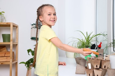 Little girl adding soil into peat pots on window sill indoors. Growing vegetable seeds
