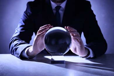 Photo of Businessman using crystal ball to predict future at table, closeup