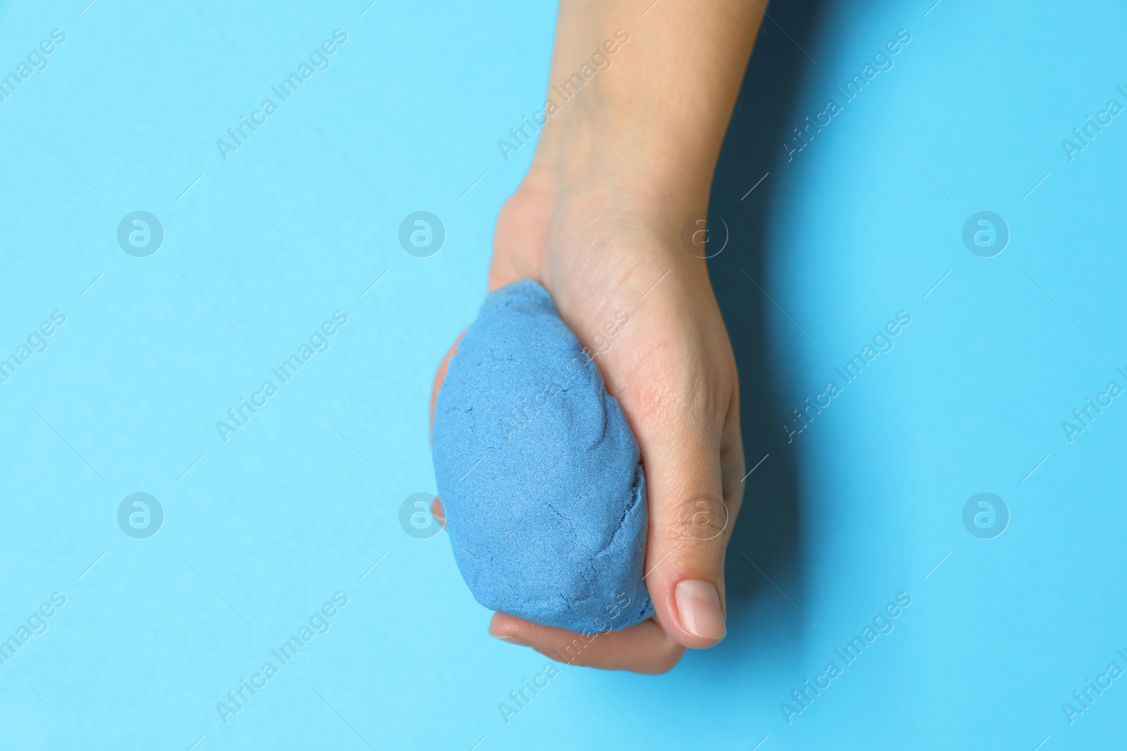 Photo of Woman playing with kinetic sand on light blue background, top view