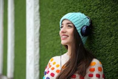 Photo of Beautiful young woman listening to music with headphones near grass wall. Space for text