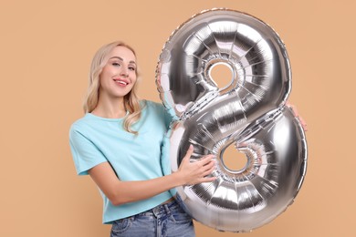 Photo of Happy Women's Day. Charming lady holding balloon in shape of number 8 on beige background