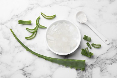 Photo of Aloe vera gel and slices of plant on white marble table, flat lay