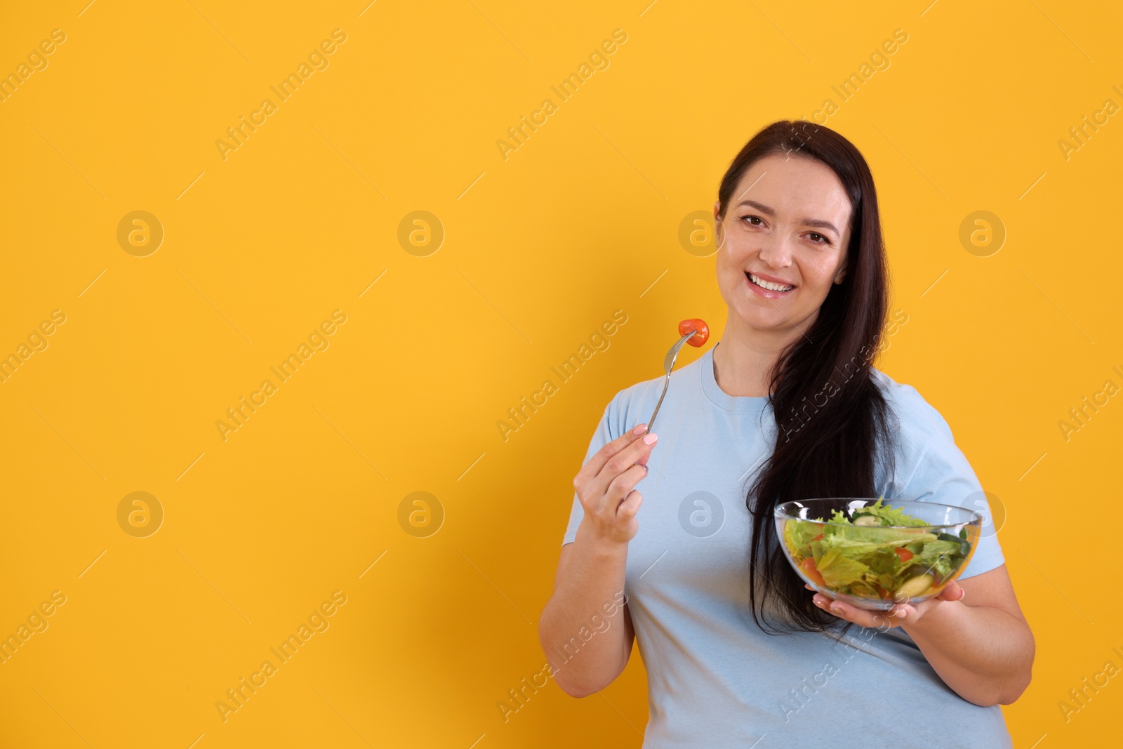 Photo of Beautiful overweight woman eating salad on yellow background, space for text. Healthy diet