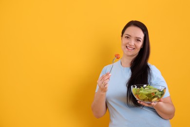 Beautiful overweight woman eating salad on yellow background, space for text. Healthy diet