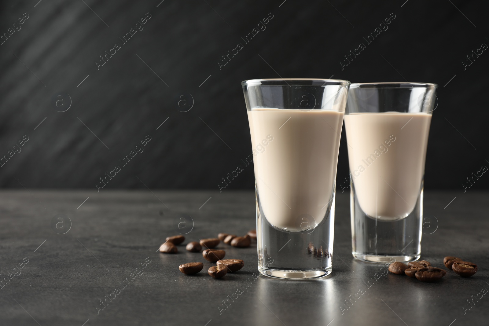 Photo of Coffee cream liqueur in glasses and beans on grey table, closeup. Space for text