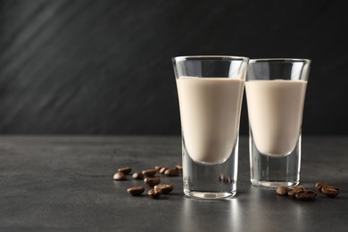 Photo of Coffee cream liqueur in glasses and beans on grey table, closeup. Space for text