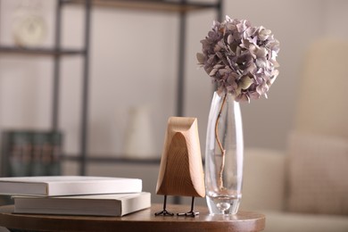 Photo of Vase with beautiful dried hydrangea, wooden bird and books on table in living room