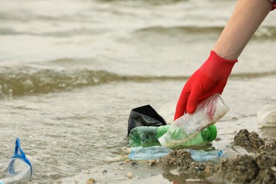 Woman in gloves collecting garbage on beach, closeup