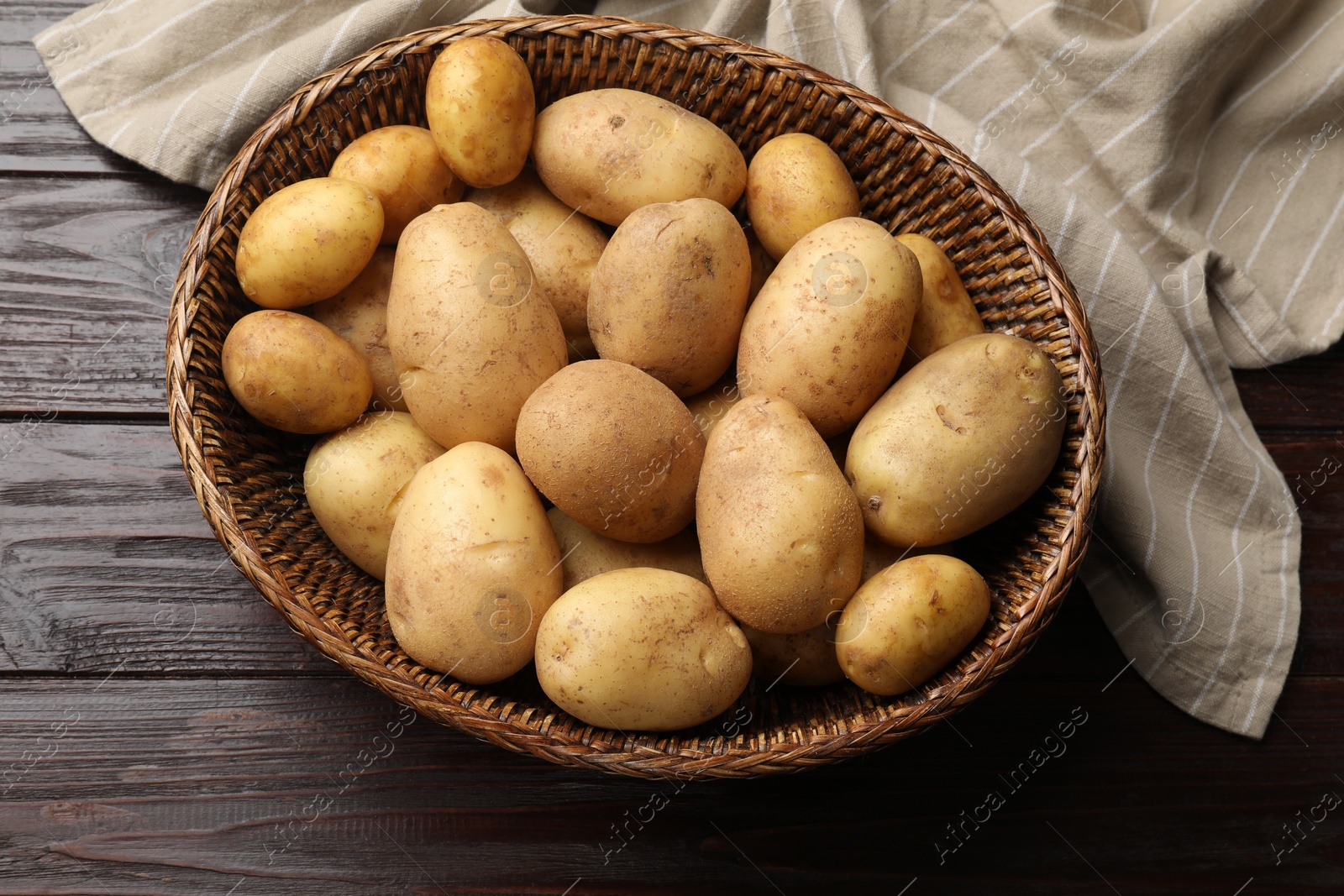 Photo of Raw fresh potatoes in wicker basket on wooden table, top view