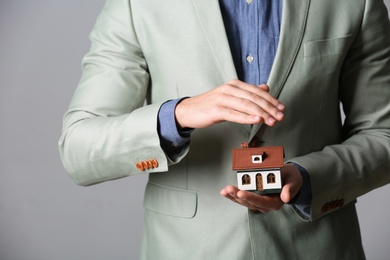 Photo of Male agent covering house model on grey background, closeup. Home insurance