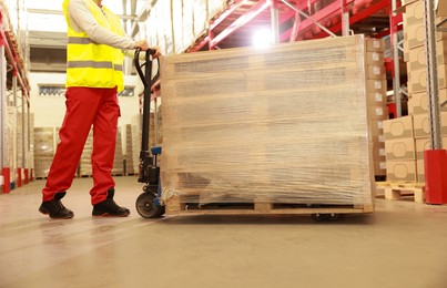 Image of Worker moving wrapped wooden pallets with manual forklift in warehouse, closeup