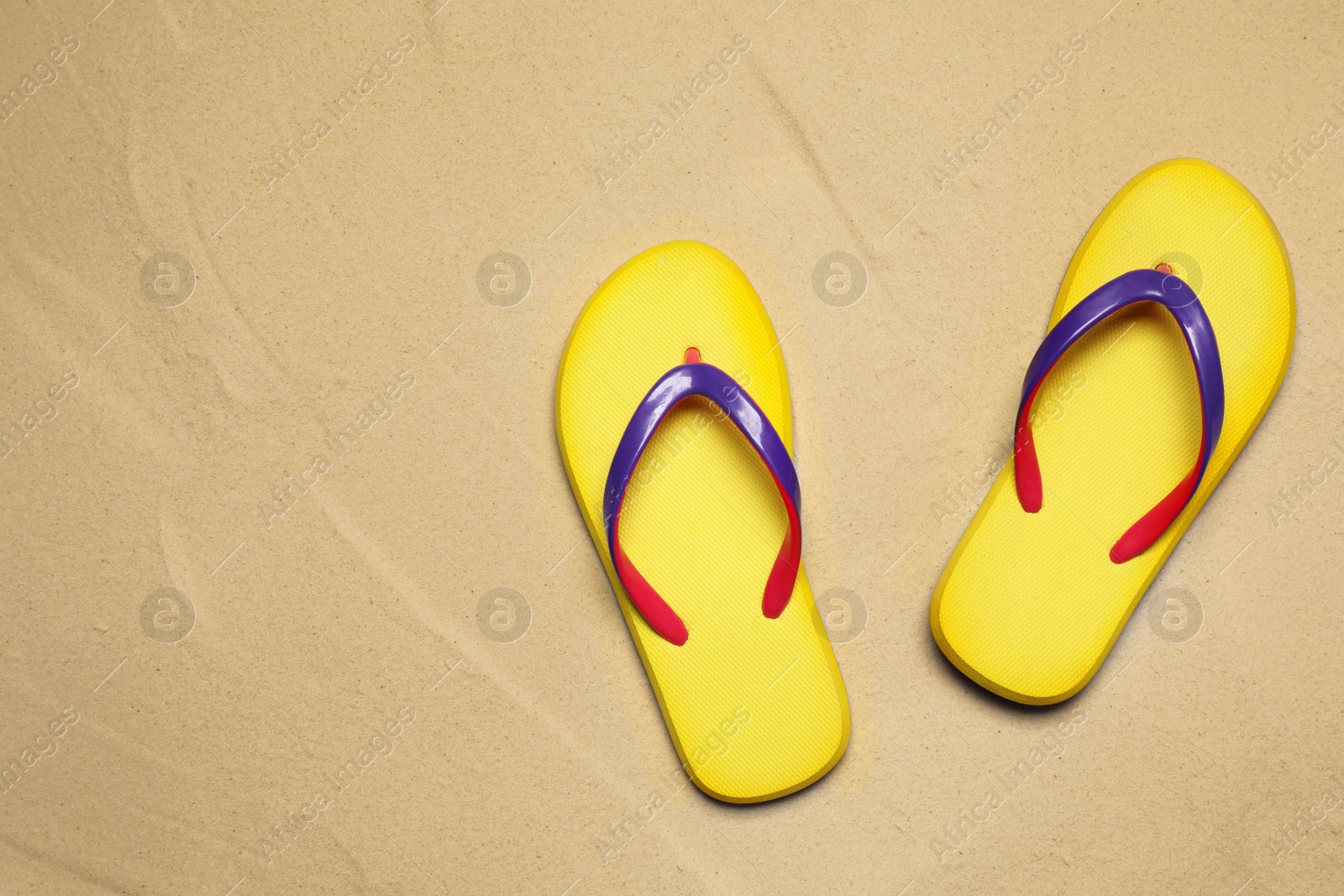 Photo of Yellow flip flops on sand, flat lay. Beach accessory