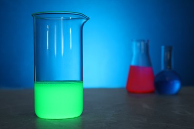 Laboratory glassware with luminous liquids on table against light blue background, selective focus. Space for text