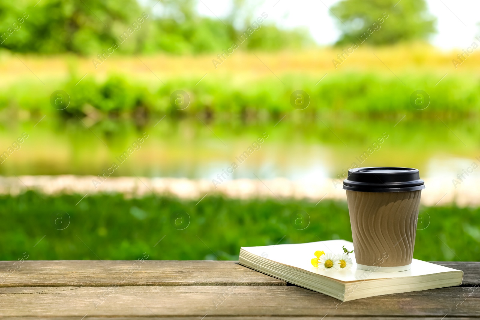 Photo of Paper coffee cup, flowers and book on wooden table outdoors, space for text