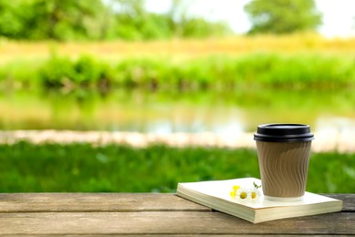 Photo of Paper coffee cup, flowers and book on wooden table outdoors, space for text