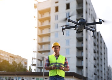 Photo of Builder operating drone with remote control at construction site, focus on quadcopter. Aerial survey