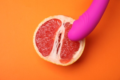 Half of grapefruit and purple vibrator on orange background, flat lay. Sex concept