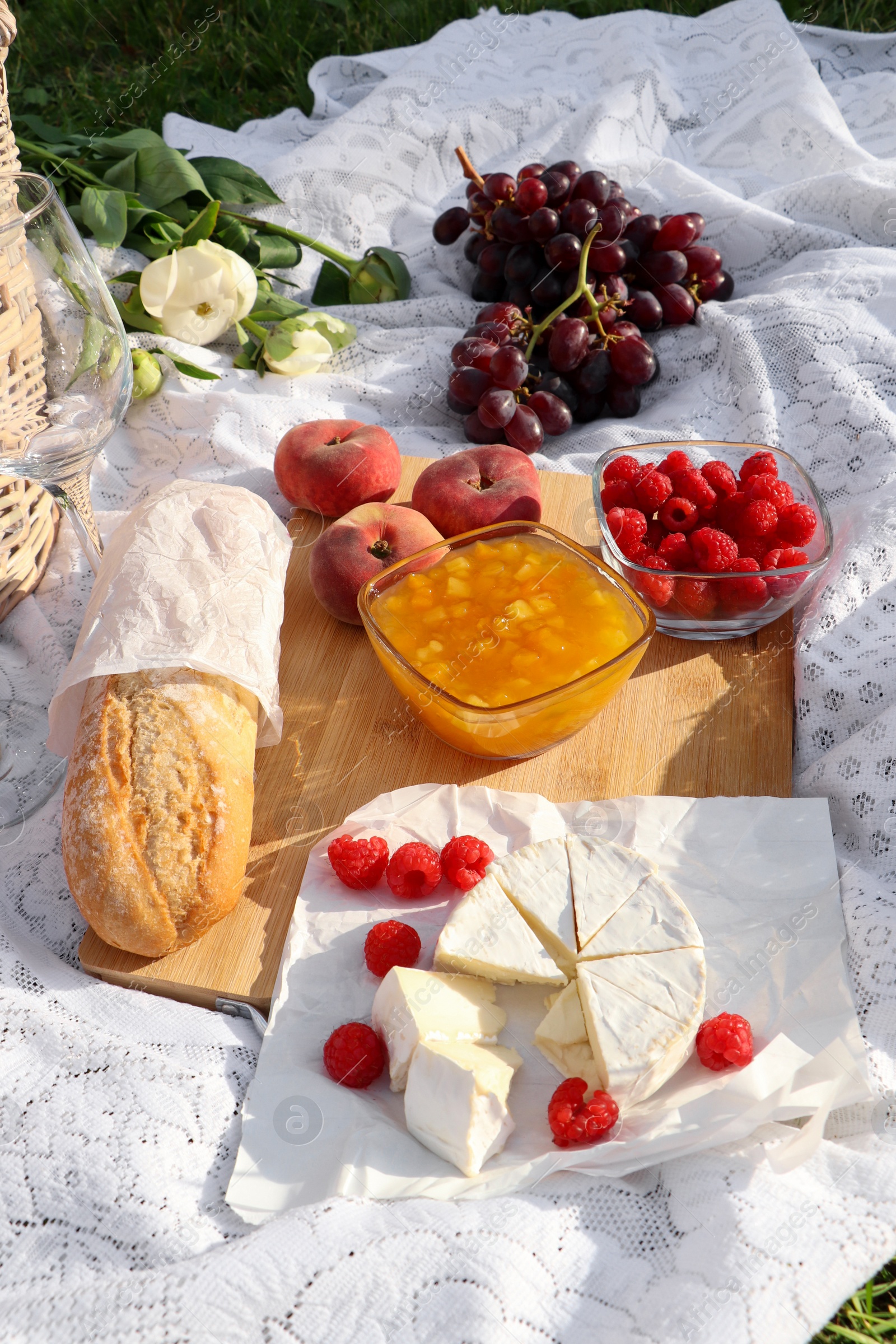 Photo of Picnic blanket with tasty food and flowers outdoors