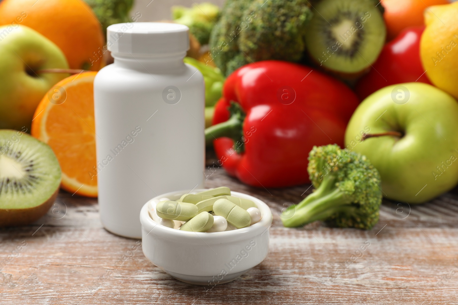 Photo of Dietary supplements. Plastic bottle, pills in bowl and food products on wooden table