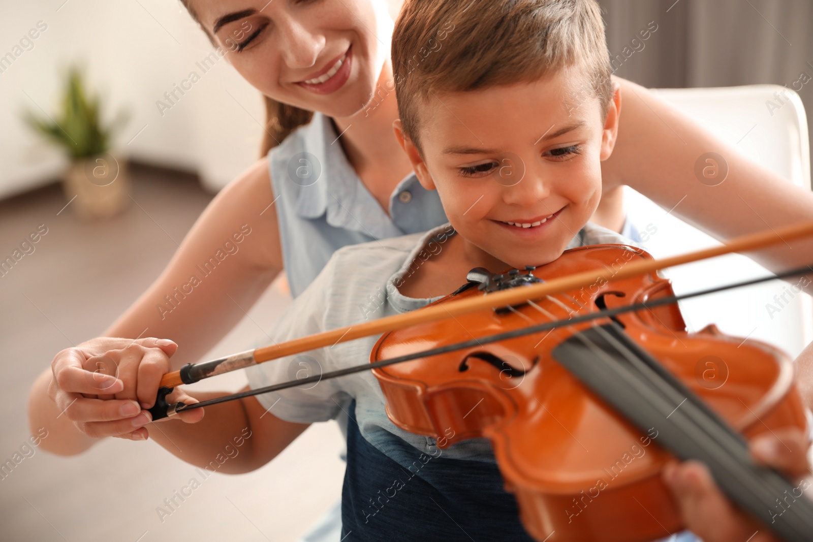 Photo of Young woman teaching little boy to play violin indoors