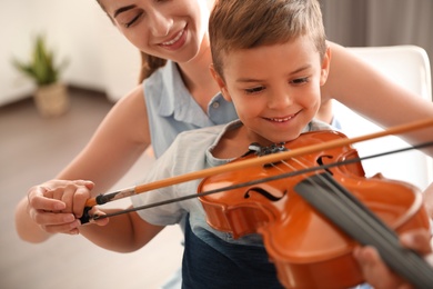 Young woman teaching little boy to play violin indoors