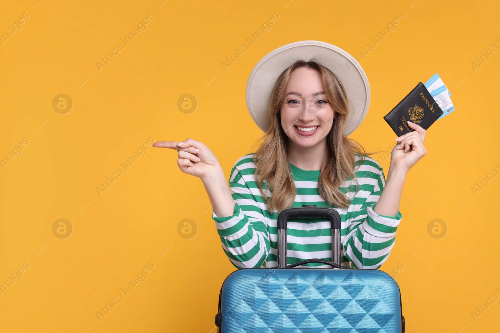 Photo of Happy young woman with passport, ticket and suitcase pointing at something on yellow background, space for text