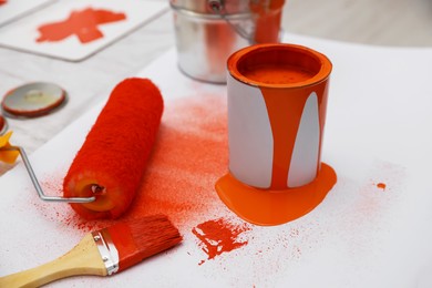Photo of Cans of orange paint, brush and roller on white table indoors