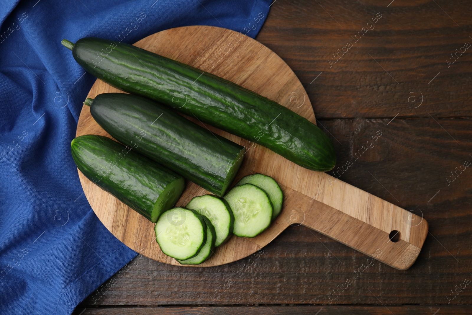 Photo of Fresh whole and cut cucumbers on wooden table, top view