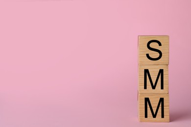 Photo of Wooden cubes with abbreviation SMM (Social media marketing) on pink background. Space for text