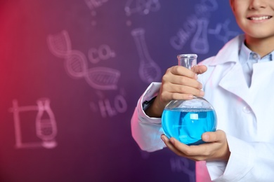 Schoolboy holding Florence flask against blackboard with written chemistry formulas, closeup. Space for text