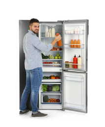 Photo of Young man taking juice out of refrigerator on white background