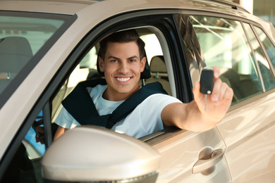 Photo of Happy man with car key sitting in modern auto at dealership