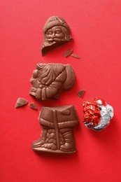 Photo of Broken chocolate Santa Claus and foil wrapper on red background, flat lay