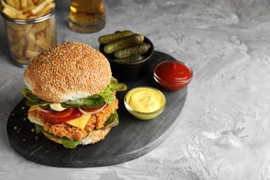 Photo of Delicious burger with crispy chicken patty and sauces on grey table