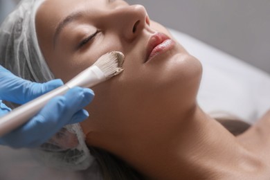 Photo of Cosmetologist applying mask on client's face in spa salon, closeup