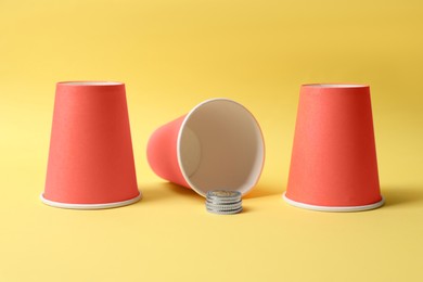 Photo of Three red cups and coins on yellow background. Thimblerig game