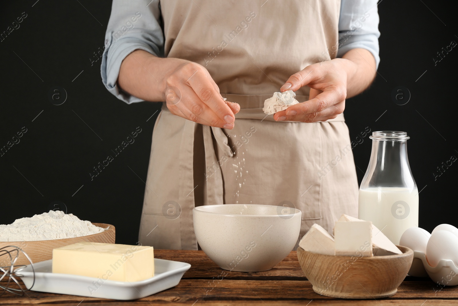Photo of Woman with compressed yeast and dough ingredients at wooden table, closeup