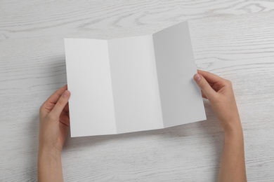 Photo of Woman with blank brochure on wooden background, above view. Mock up for design