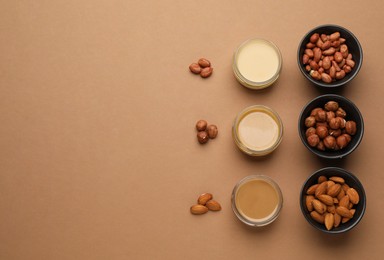 Different types of delicious nut butters and ingredients on brown background, flat lay. Space for text